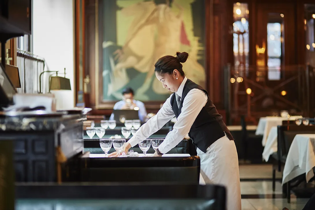 Waitress setting the tables in the Delaunay with lots of glassware and green leather seats
